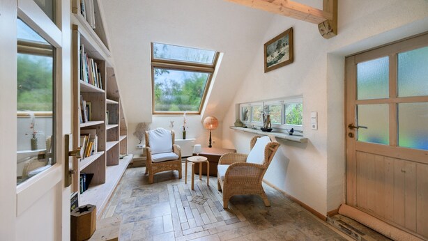 Une pièce chaleureuse avec un plafond en pente, des étagères intégrées, des meubles en osier, une petite table et une porte dont les panneaux sont en verre dépoli.