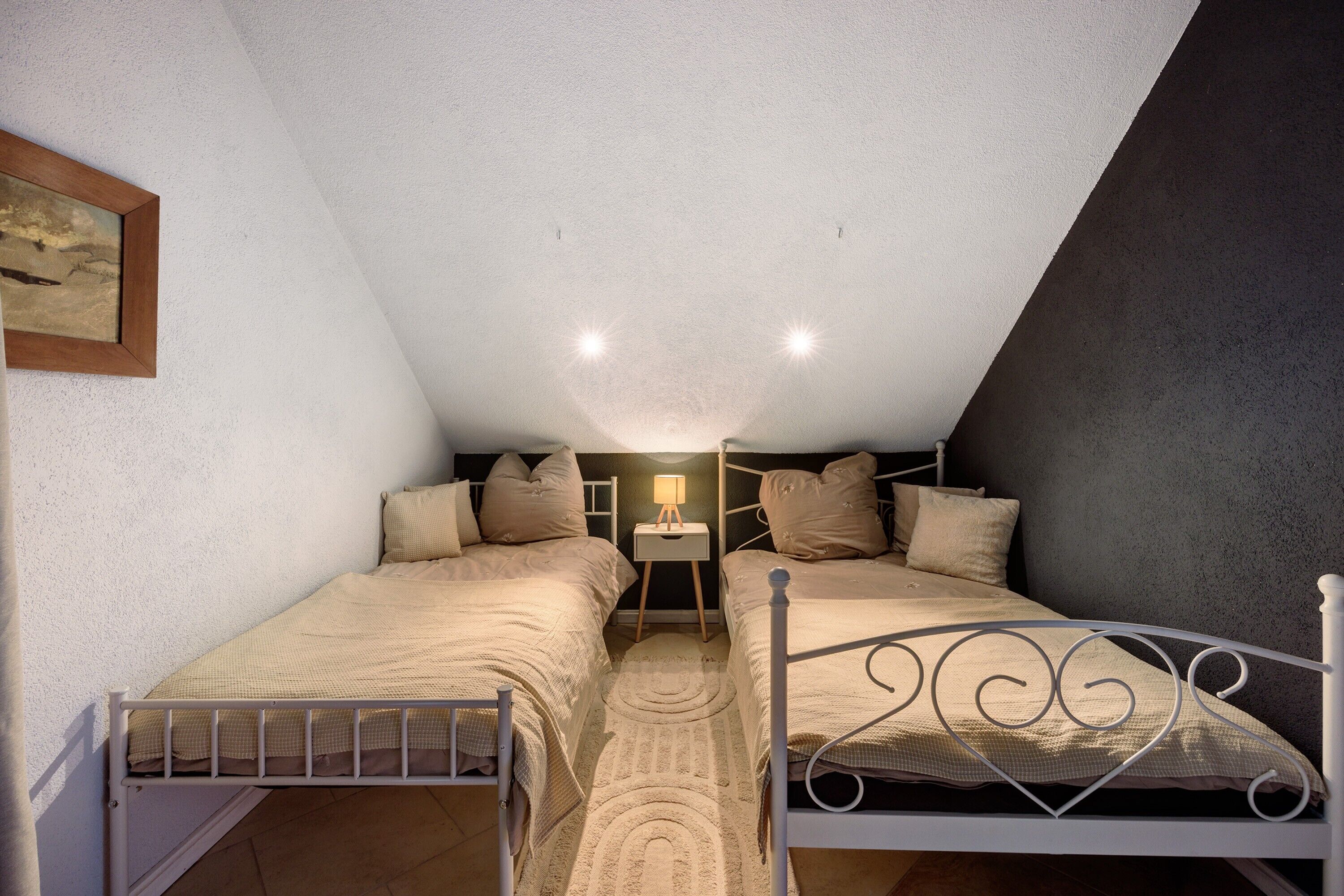 A bedroom with two beds, a nightstand, a lamp, and a framed picture on the wall.
