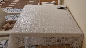 Een zithoek met een tafel, bedekt met een geribbelde witte tafelkleed, een stoel en een afstandsbediening op de tafel.