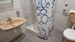 Een badkamer met een wastafel, toilet, douche en een glazen plank.