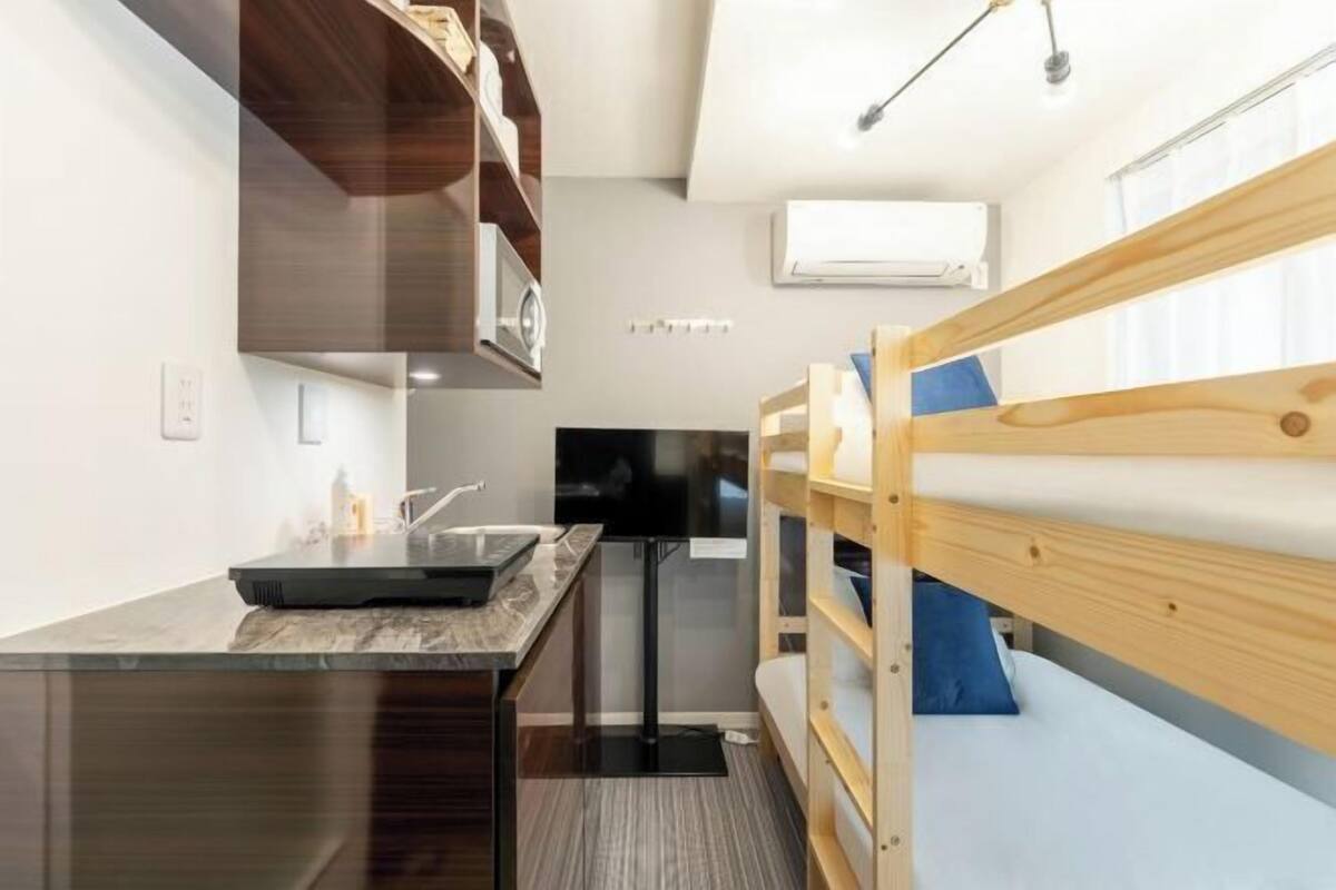 A compact room with bunk beds, a kitchenette, a flat-screen TV, and a ceiling-mounted air conditioning unit.
