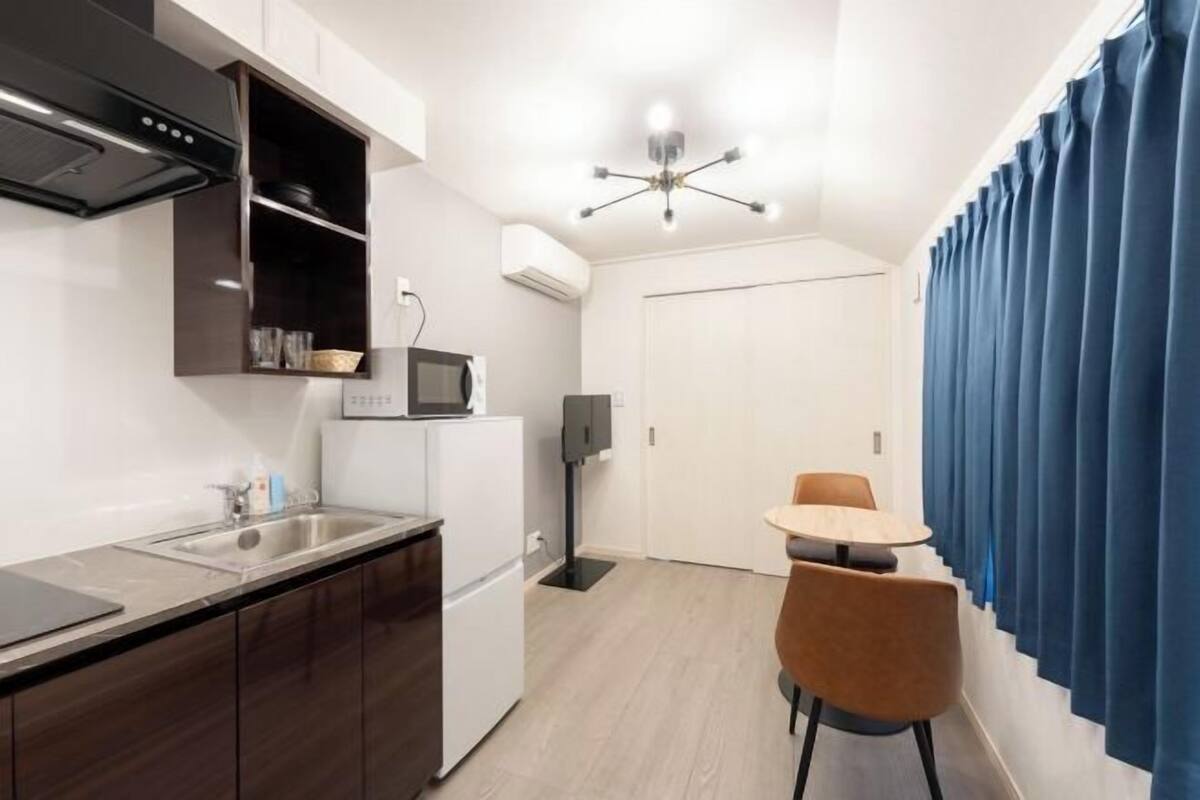 A compact kitchen with a microwave, a sink, and a small refrigerator. There is a dining area with a table and chairs.