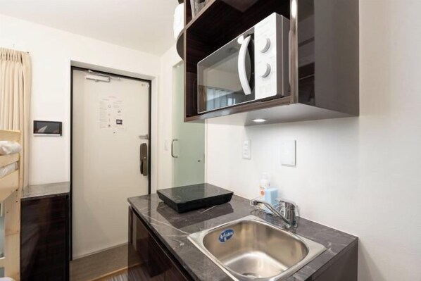 A compact kitchen with a built-in microwave, a stainless steel sink, and a small countertop. - LaVie Yotsuya (Tokyo)