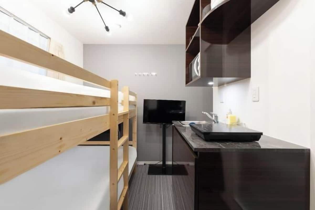 A bunk bed, a flat-screen TV, a sink, and a microwave in a compact kitchen area.