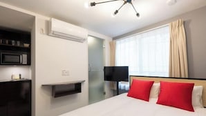 A hotel room with a bed, a TV, an air conditioning unit, a microwave, and a window with curtains. - LaVie Yotsuya (Tokyo)