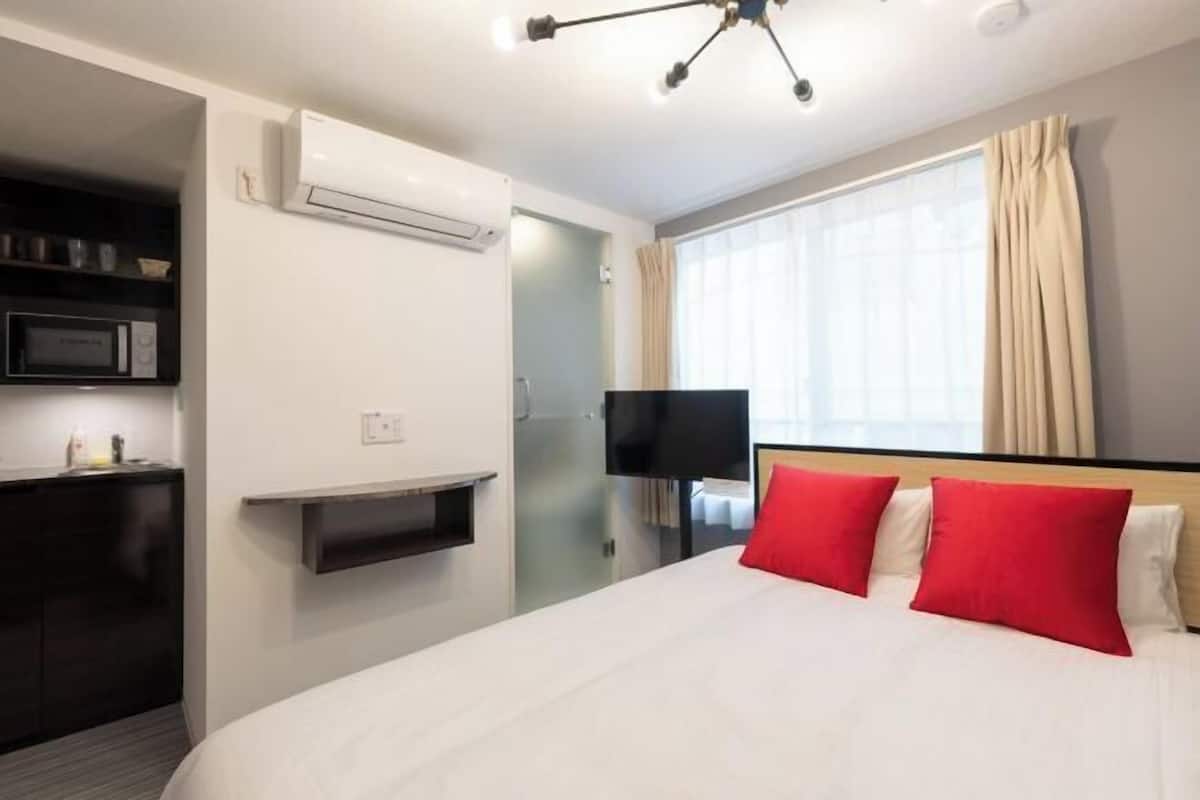 A hotel room with a bed, a TV, an air conditioning unit, a microwave, and a window with curtains.