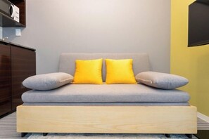 A sofa with two pillows, a wooden bench, and a wall-mounted TV. - LaVie Yotsuya (Tokyo)