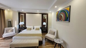 A hotel room with a large bed, two bedside tables with lamps, a small round table, two armchairs, and a colorful abstract painting on the wall. - Goha Addis Hotel (Addis Ababa)