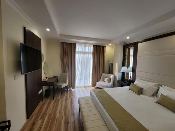 Una habitación de hotel con una cama grande, un escritorio con una silla, un televisor y una ventana con cortinas.
