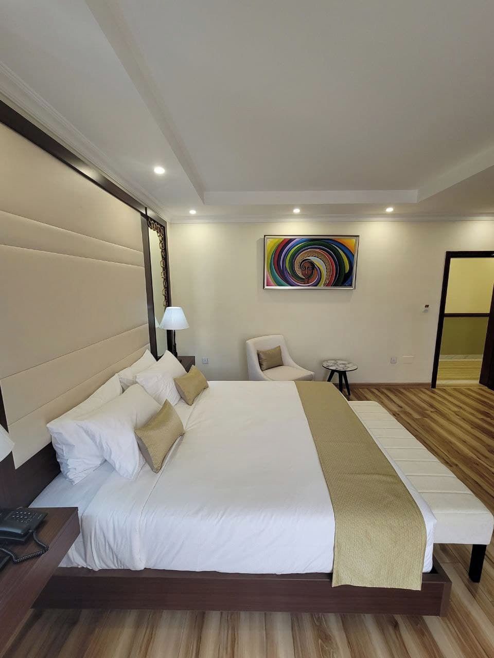 A modern hotel room with a large bed, a bedside table with a lamp, a chair, and a small table.