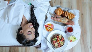 A person lying on a bed with a tray of food including croissants, waffles, and fruit. - Goha Addis Hotel (Addis Ababa)