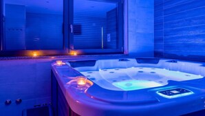 Uma área de spa moderna com uma banheira de hidromassagem iluminada por luzes azuis, porta de vidro de entrada e parede revestida de azulejos.