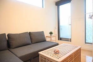 A modern living room with a grey sofa, a wooden coffee table, and a small side table with a plant. - Nishiikebukuro Pure Gray Villa (Tokyo)