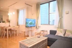 Una sala de estar moderna con un sofá gris, una mesa de centro de madera, un televisor sobre un mueble bajo y una zona de comedor con mesa y sillas.