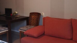 Uma sala de estar com um sofá vermelho, uma cadeira de madeira e uma pequena mesa com um vaso e um livro.