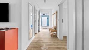 Un couloir doté d’un plancher en bois, de murs blancs et d’un téléviseur fixé au mur, sur le côté gauche.
