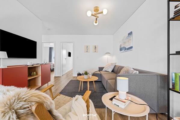 A modern living room with a flat-screen TV, a red entertainment unit, a grey sofa, a coffee table, and a bookshelf.
