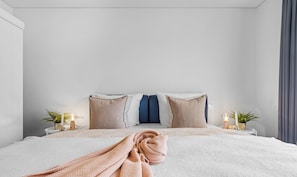 A neatly made bed with a folded blanket, two bedside tables with lamps, and a potted plant on each side. - Sprotte 1 - Terrace, Infrared Sauna, and Fireplace, Close to the Beach (Olpenitz)