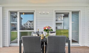 An outdoor dining area with a table set for two, a vase with flowers, and a view of the neighborhood.