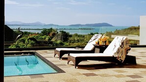 Zona junto a la piscina con sillones y vista al mar.