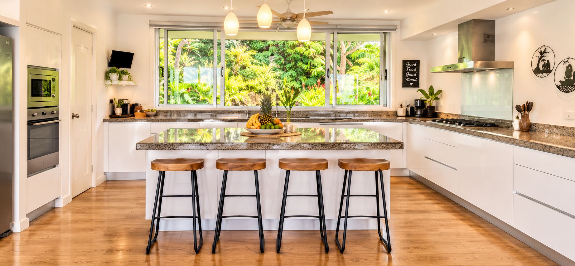 A modern kitchen with a central island, bar stools, a built-in oven, and a large window offering a view of greenery.