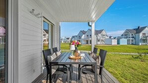 A covered outdoor patio with a table and chairs, overlooking a residential area with houses.