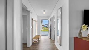 A hallway with a wooden bench, a wooden staircase, and a view of the outside.