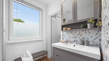 Een moderne badkamer met een groot raam, een bankje, een wastafel met spiegel en een betegelde spatwand.