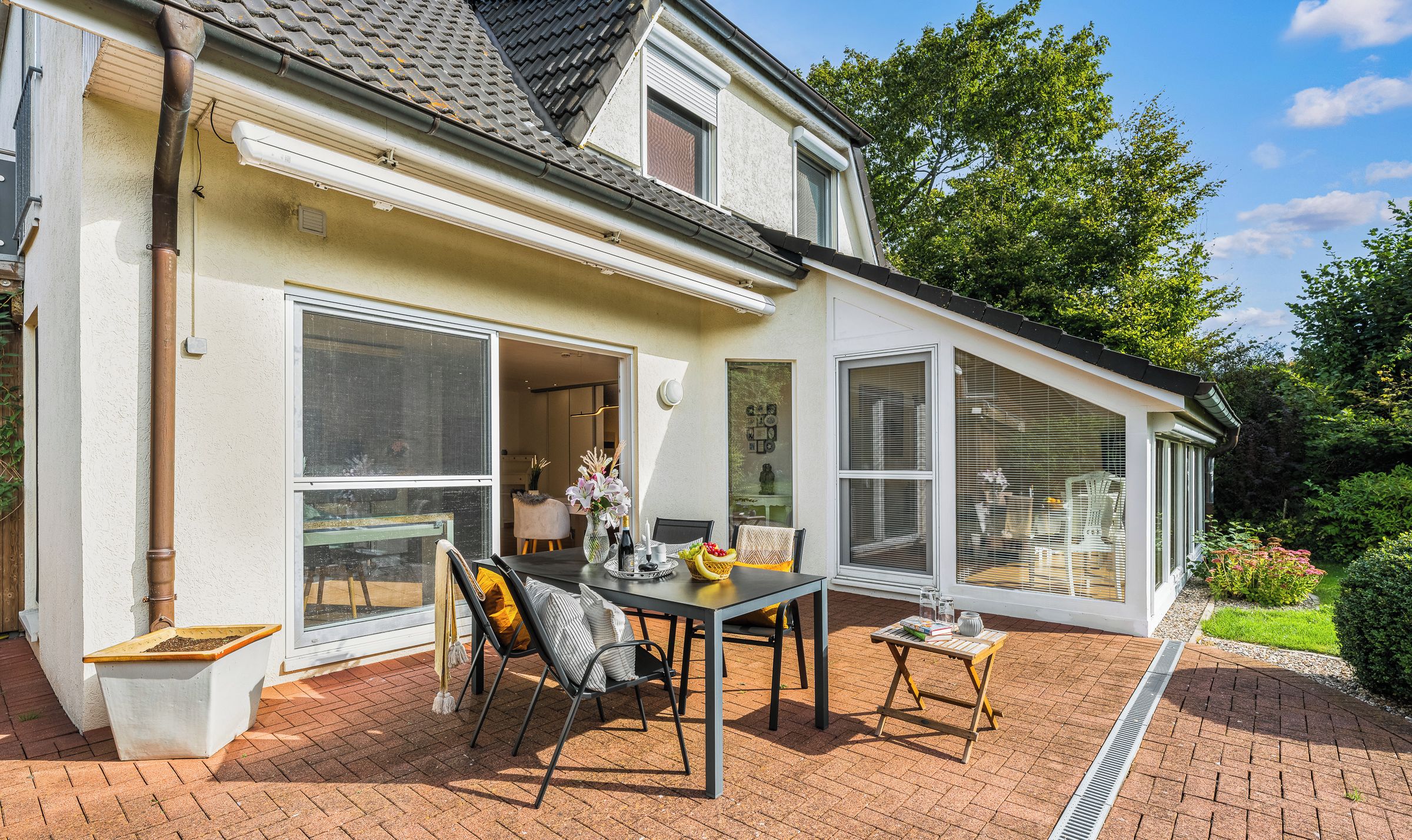 Een huis met een patio, compleet met een tafel, stoelen, een raam en een kleine tuin.