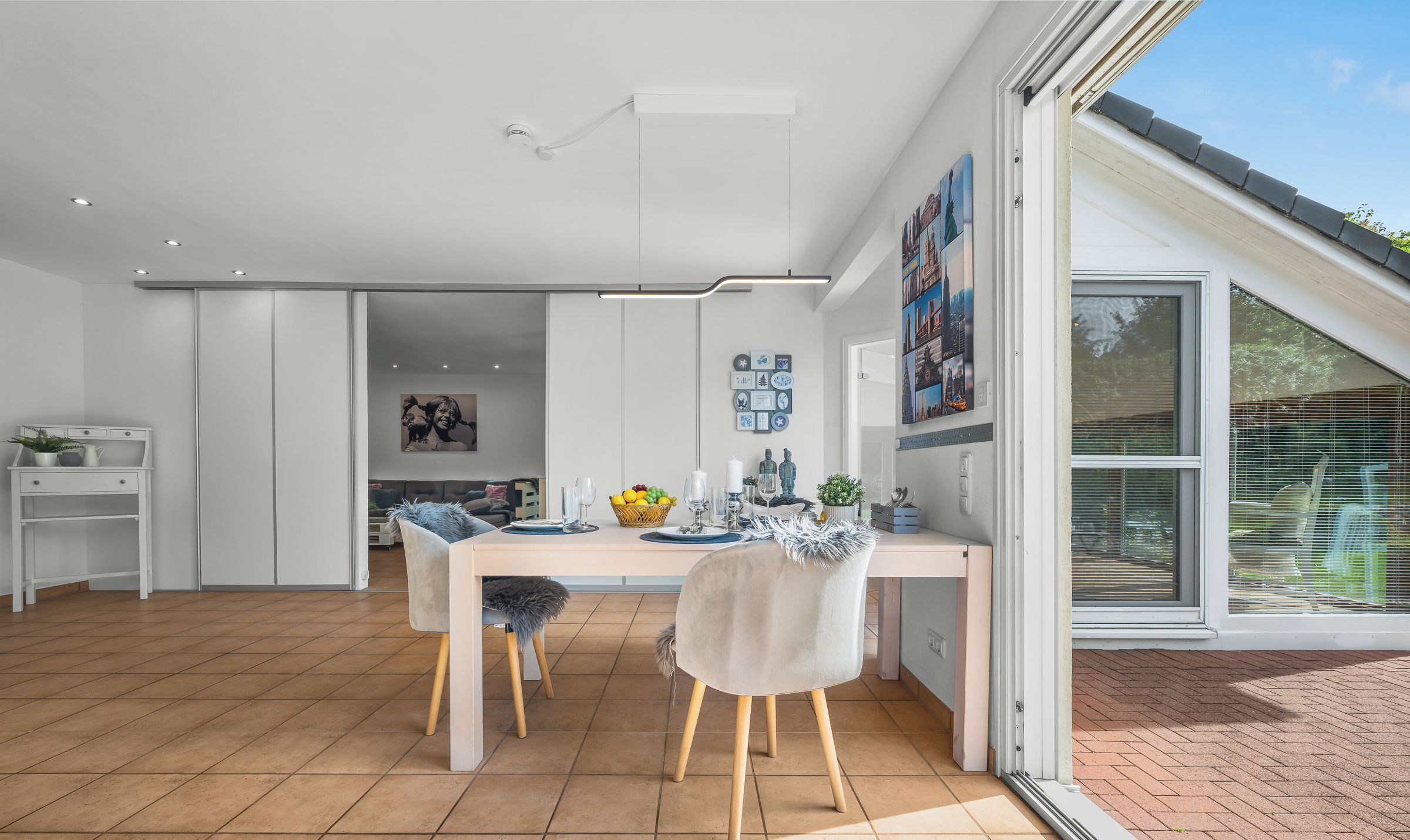 Una cocina moderna con armarios blancos, una mesa de comedor con sillas y un ventanal con persianas.