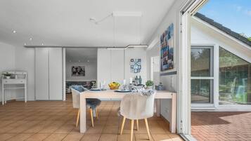 Una cocina moderna con armarios blancos, una mesa de comedor con sillas y un ventanal con persianas.