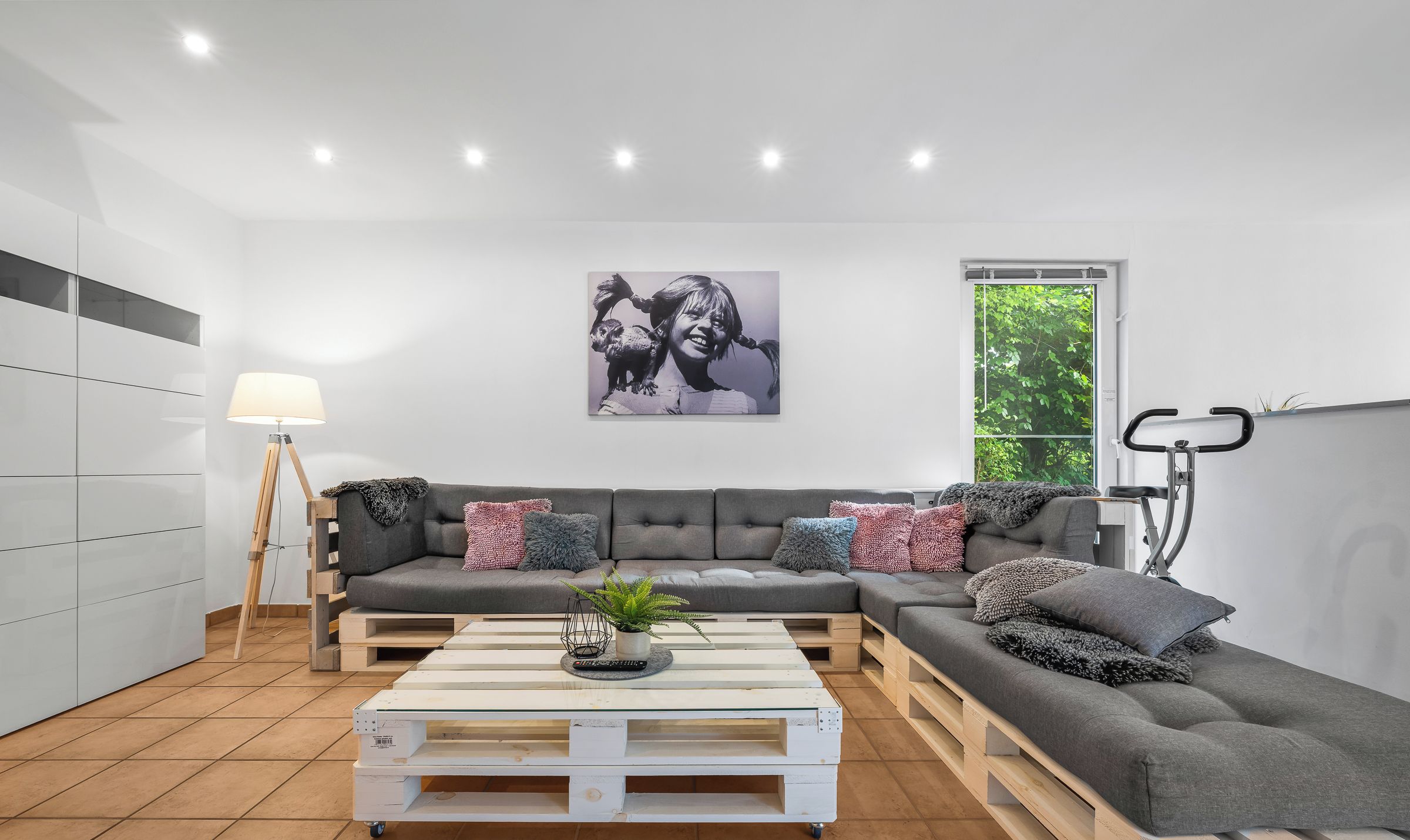 Ein modernes Wohnzimmer mit einem grauen Ecksofa, einem Couchtisch aus Holz und Weiß sowie einer Stehlampe.