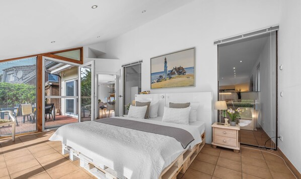 Un dormitorio con una cama grande, una mesita de noche, un cuadro y una puerta corredera que da a un espacio exterior.