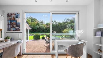 Ein modernes Zimmer mit einem großen Schiebeglastür, die zu einem Garten führt, einem Schreibtisch mit Stuhl und einem Bücherregal.
