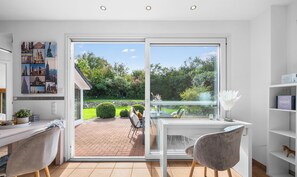 Una habitación moderna con un amplio ventanal corredera que da a un jardín, un escritorio con una silla y una estantería.