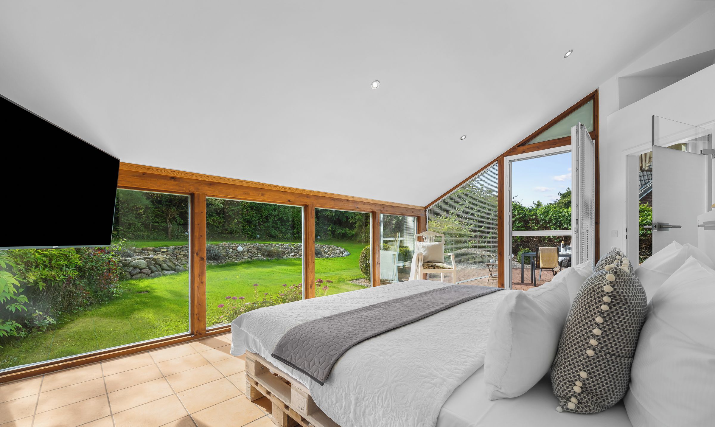 Een slaapkamer met een groot bed, uitzicht op een tuin en een schuifdeur naar buiten.