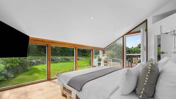 Een slaapkamer met een groot bed, uitzicht op een tuin en een schuifdeur naar buiten.