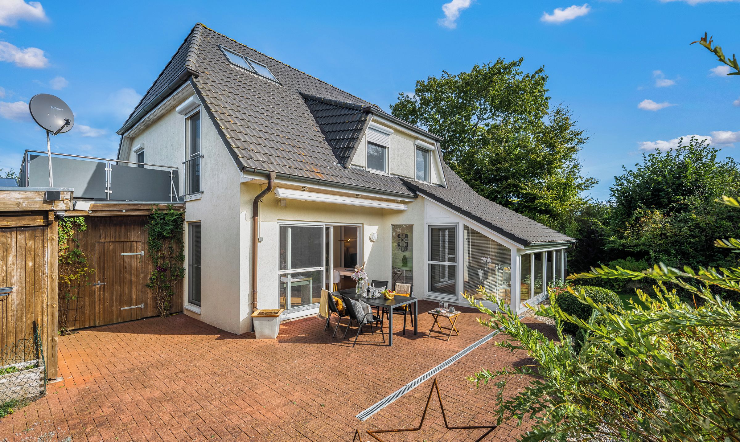 Ein zweistöckiges Haus mit Ziegelterrasse, großen Fenstern und einer Satellitenschüssel.