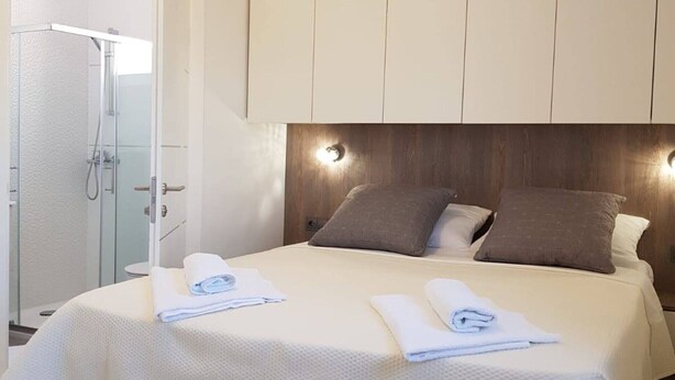 Een hotelkamer met een bed, twee kussens, een hoofdbord met verlichting en een douche.