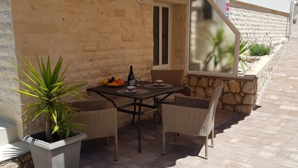 Une terrasse extérieure avec une table et des chaises, un pot de fleurs et une fenêtre donnant sur un mur en pierre.