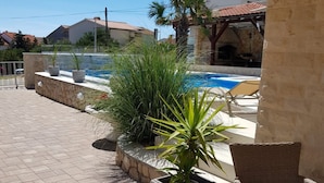Un espace piscine agrémenté d’un mur en pierre, de plantes en pot et d’une chaise longue.