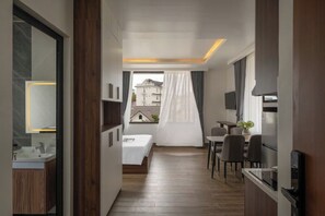A modern hotel room with a wooden floor, a bed, a small table, a chair, a TV, and a window with curtains. - Anteaus Hotel & Apartment Da Lat (Dalat)