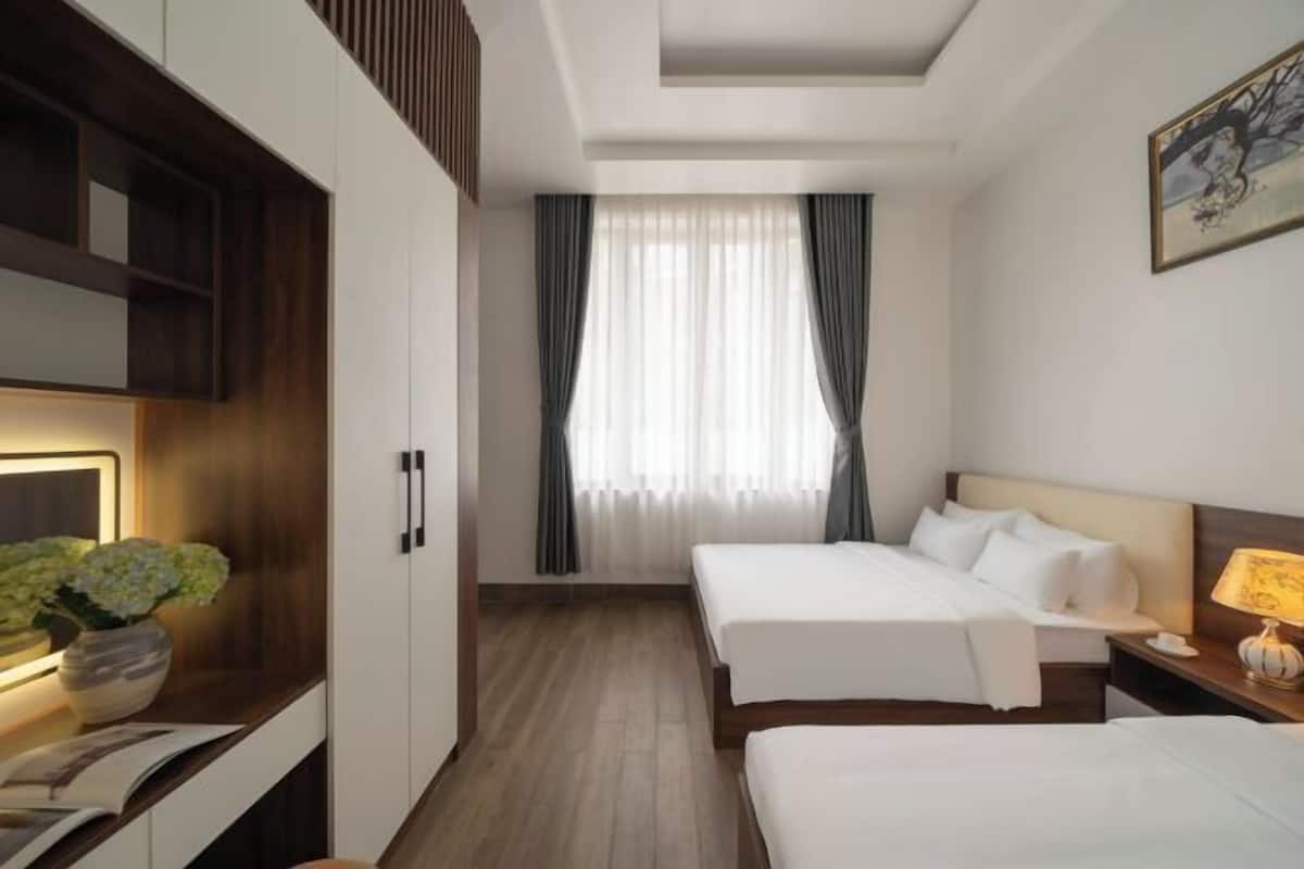 A hotel room with two beds, a desk with a lamp, a TV, and a window with curtains.
