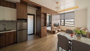 A modern kitchen with built-in appliances, a dining area with a table and chairs, and a large window with blinds. - Anteaus Hotel & Apartment Da Lat (Dalat)
