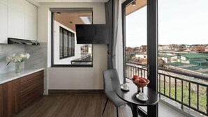 A modern kitchen with a built-in TV, a dining area with a table and chairs, and a balcony with a view of the city. - Anteaus Hotel & Apartment Da Lat (Dalat)