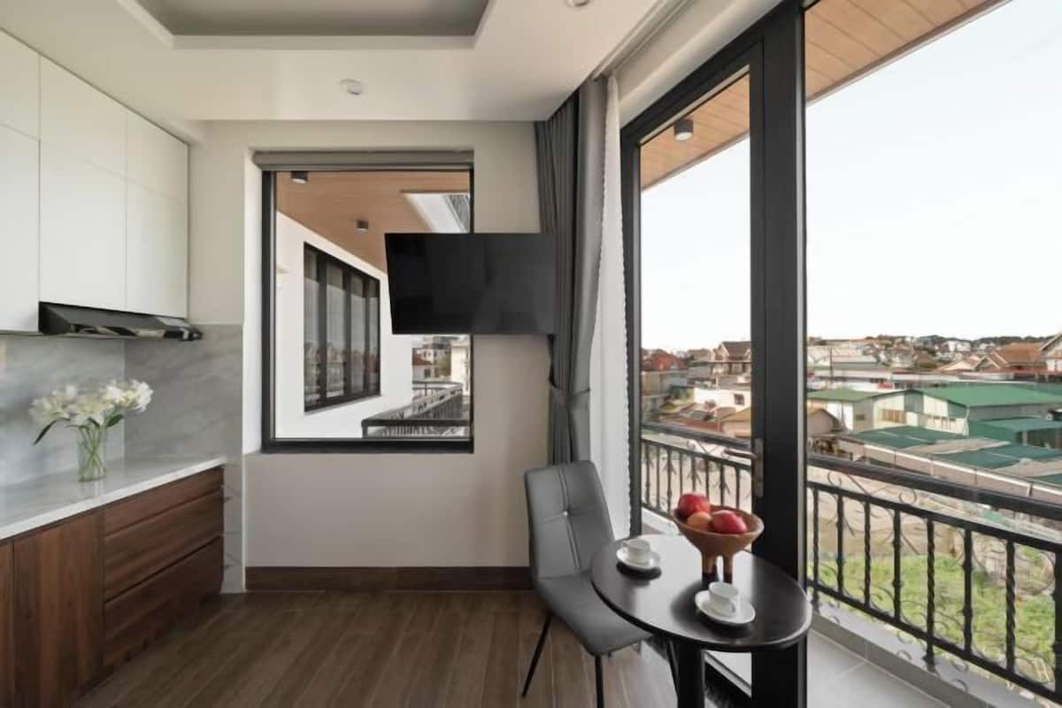 A modern kitchen with a built-in TV, a dining area with a table and chairs, and a balcony with a view of the city.