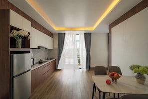 A modern kitchen with a dining area, wooden flooring, and a view through a window with curtains.