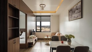 A modern room with a bed, a dining table, a sofa, and a large window with a view. - Anteaus Hotel & Apartment Da Lat (Dalat)