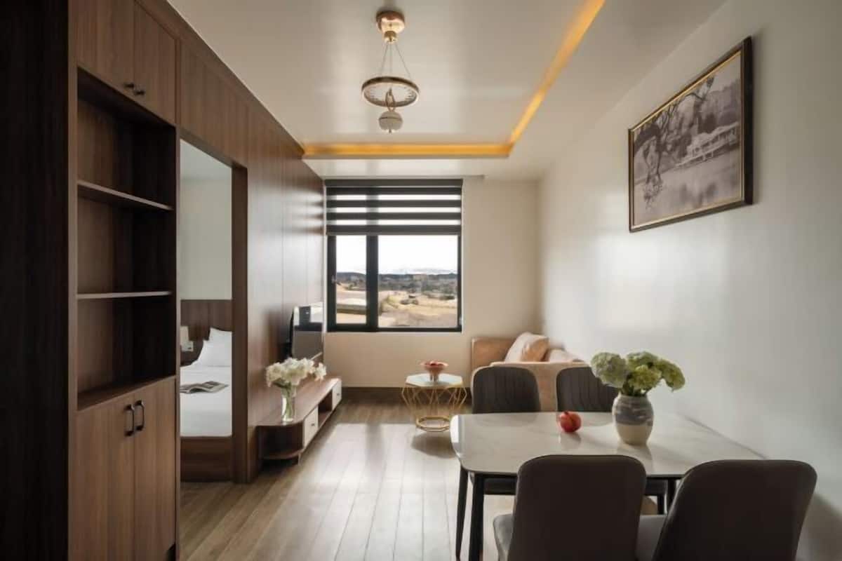 A modern room with a bed, a dining table, a sofa, and a large window with a view.