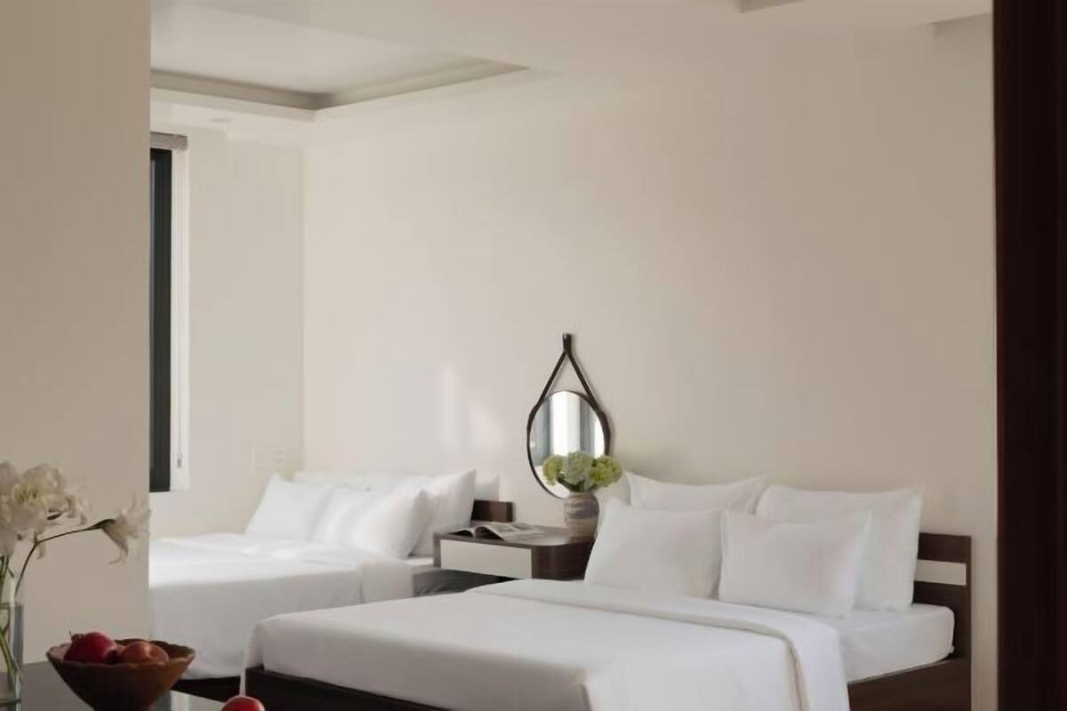 A hotel room with two beds, a bedside table, a mirror, and a vase with flowers.